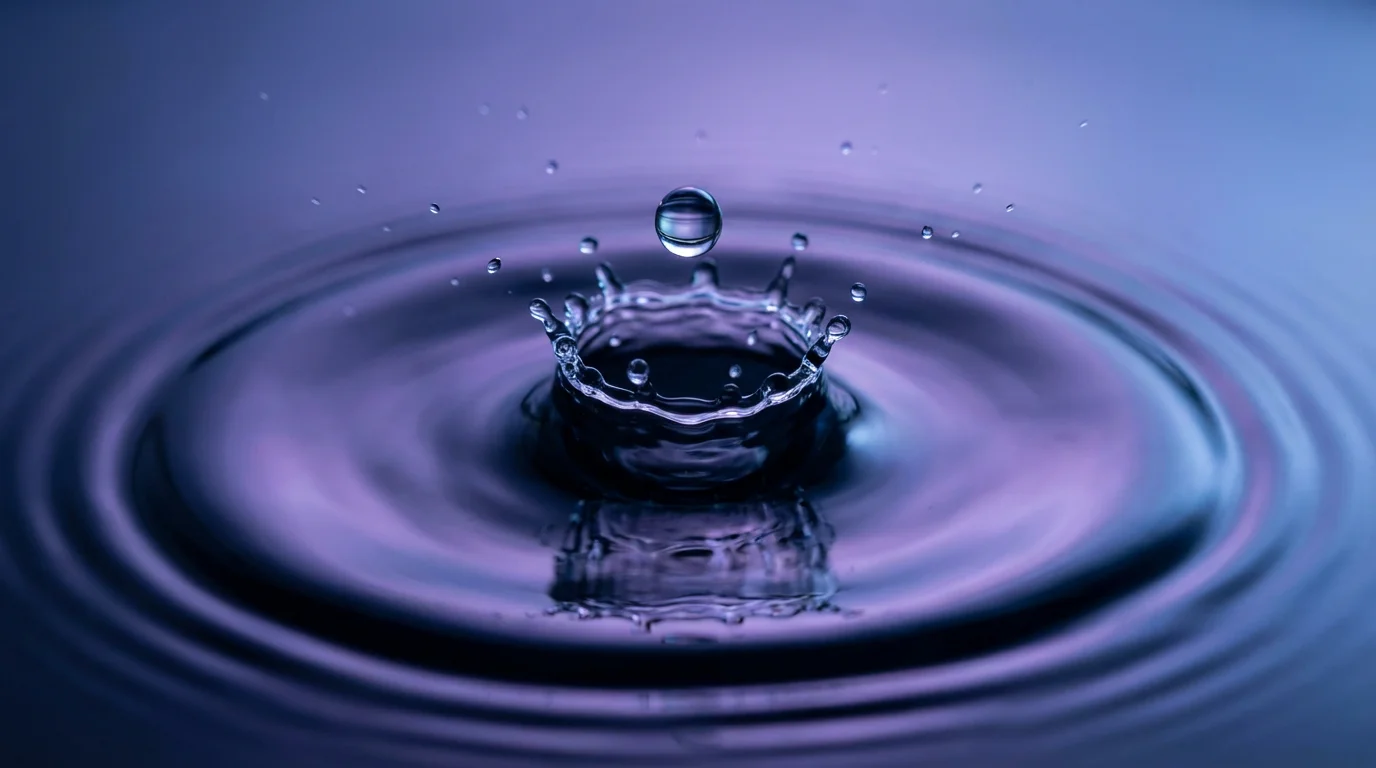 Macro photo of a water droplet hitting still water, creating perfect concentric ripples.